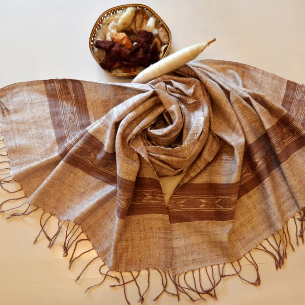A handwoven Eri silk stole in natural beige with deep brown horizontal stripes and fringe, displayed with raw silk cocoons and a spindle.